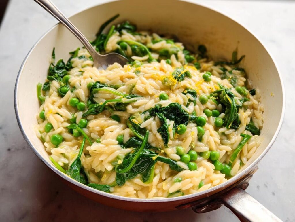 Close-up of a creamy orzo pasta dish with bright green peas and wilted spinach, a perfect 20-minute dinner idea.