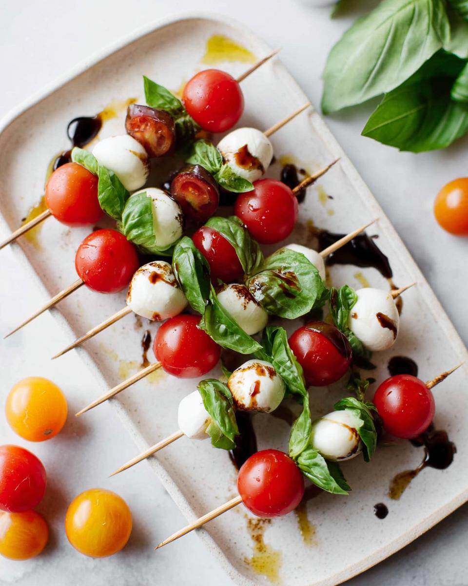 Close-up of several 5-Ingredient Caprese Skewers featuring mozzarella balls, cherry tomatoes, and basil drizzled with balsamic glaze.