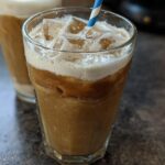 Close-up of a 5-Ingredient Starbucks Drink with ice, coffee, and a layer of cream on top, with a blue and white striped straw.