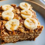 A slice of baked oatmeal topped with banana slices and a drizzle of peanut butter, perfect for breakfast ideas.