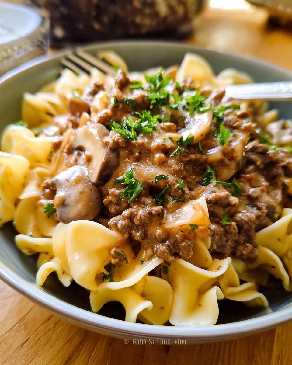 Close-up of a bowl of egg noodles topped with a creamy ground beef and mushroom sauce, garnished with parsley.