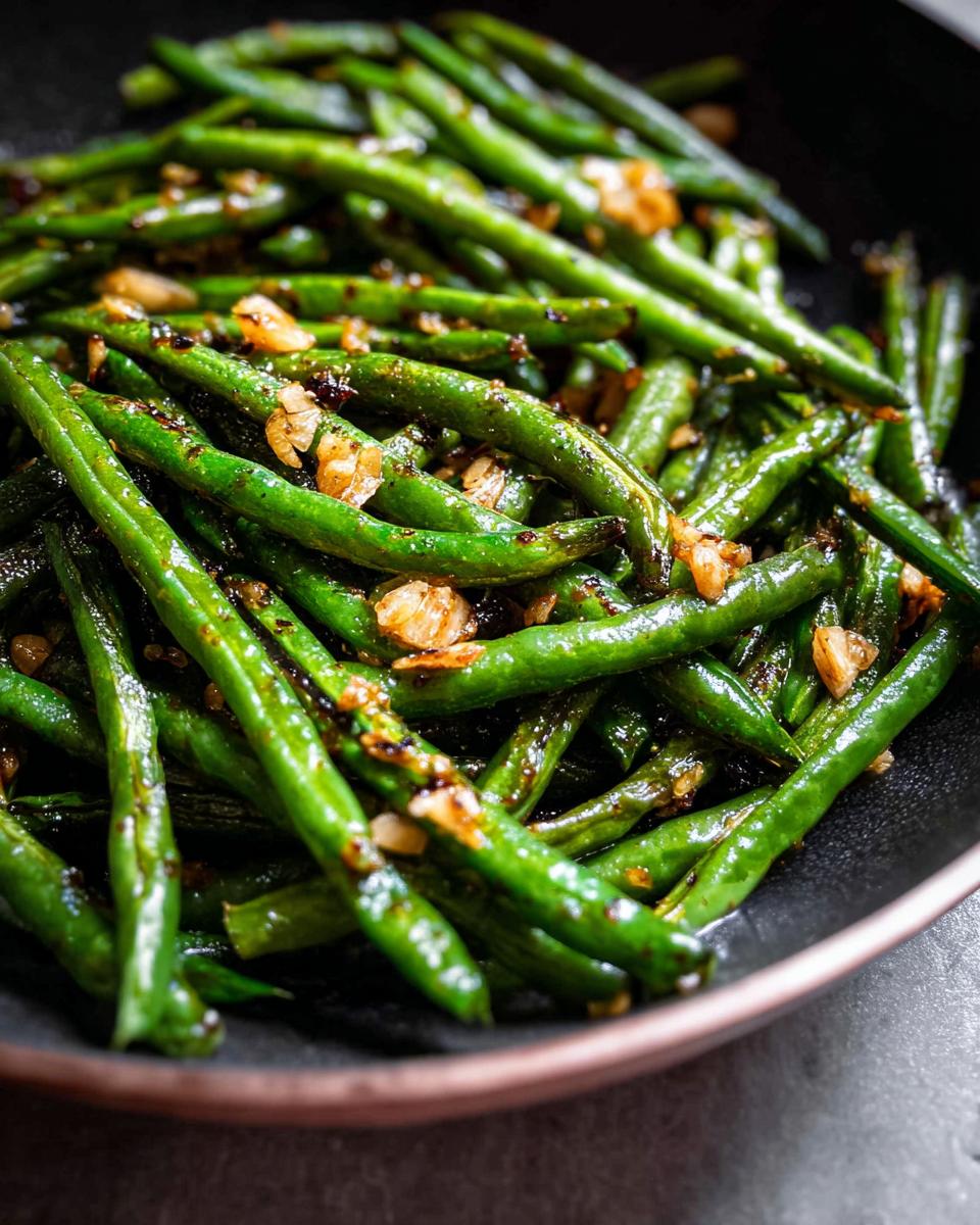 Close-up of Best Thanksgiving Green Beans 2025, glistening and tossed with garlic in a dark bowl.