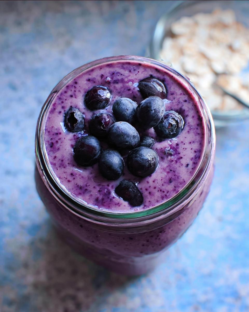 Overhead shot of a thick, purple Blueberry Oat Breakfast Smoothie topped with fresh blueberries.