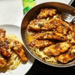 A plate of delicious chicken tenders served over spaghetti, with a skillet of more chicken and pasta in the background. Perfect for Chicken in 20 Minutes.