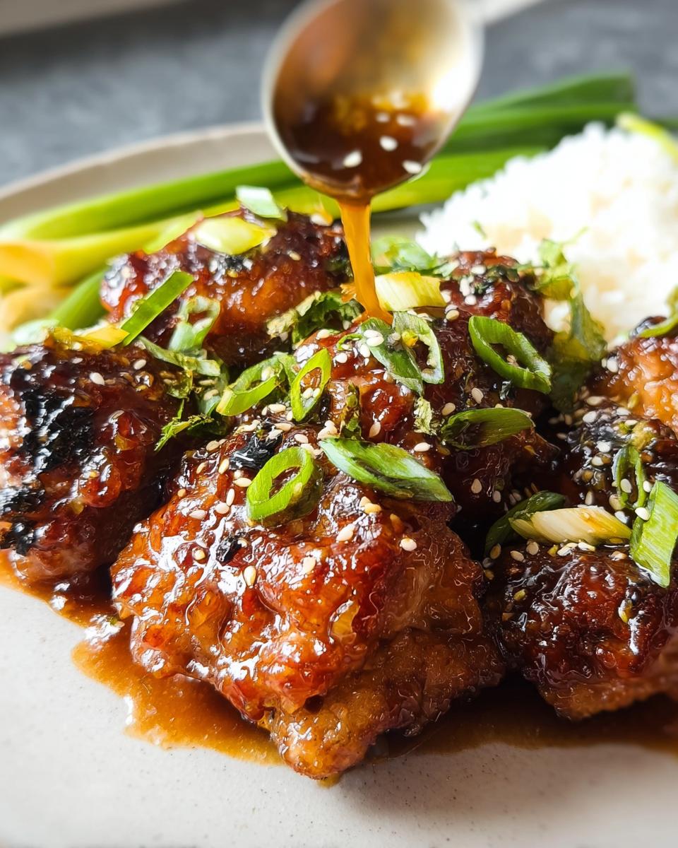 Close-up of glossy, glazed chicken thighs drizzled with sauce, topped with sesame seeds and green onions, served with rice.