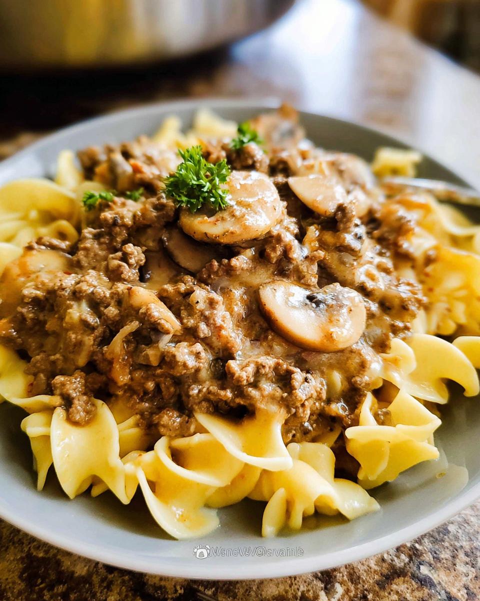 Close-up of creamy ground beef and mushroom sauce served over wide egg noodles, garnished with parsley.