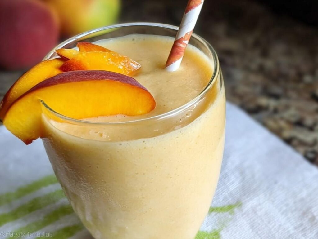 Close-up of a creamy Peach Yogurt Smoothie garnished with fresh peach slices and a striped straw.