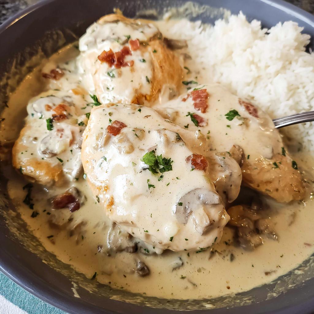 Close-up of Creamy Smothered Chicken and Rice topped with bacon bits and parsley.