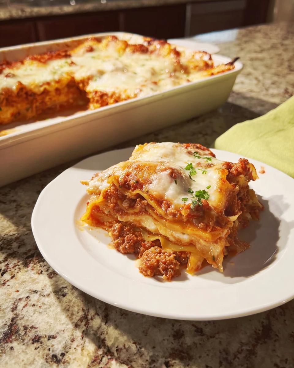 A generous slice of Easy Lasagna Dinner for Busy Families with melted cheese and meat sauce on a white plate.