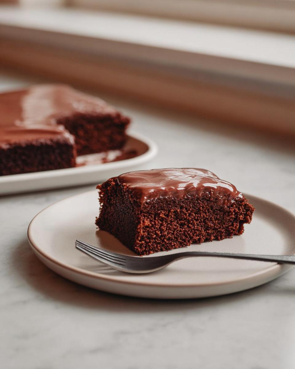 A square slice of rich, dark chocolate Easy Snacking Sheet Cake topped with glossy chocolate frosting, served on a plate with a fork.