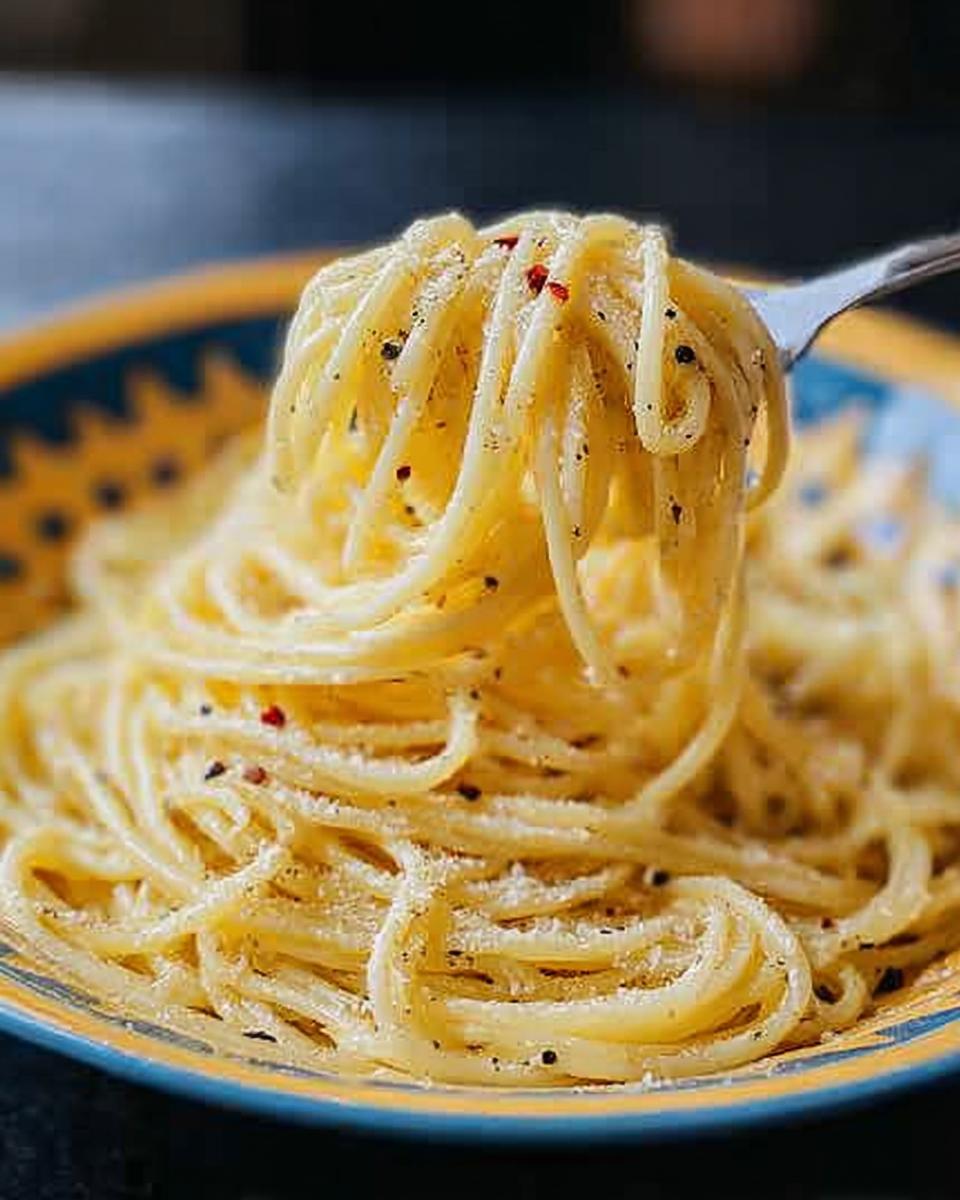 A fork lifting a swirl of spaghetti coated in Cacio e Pepe sauce, with flecks of black pepper and red pepper flakes.