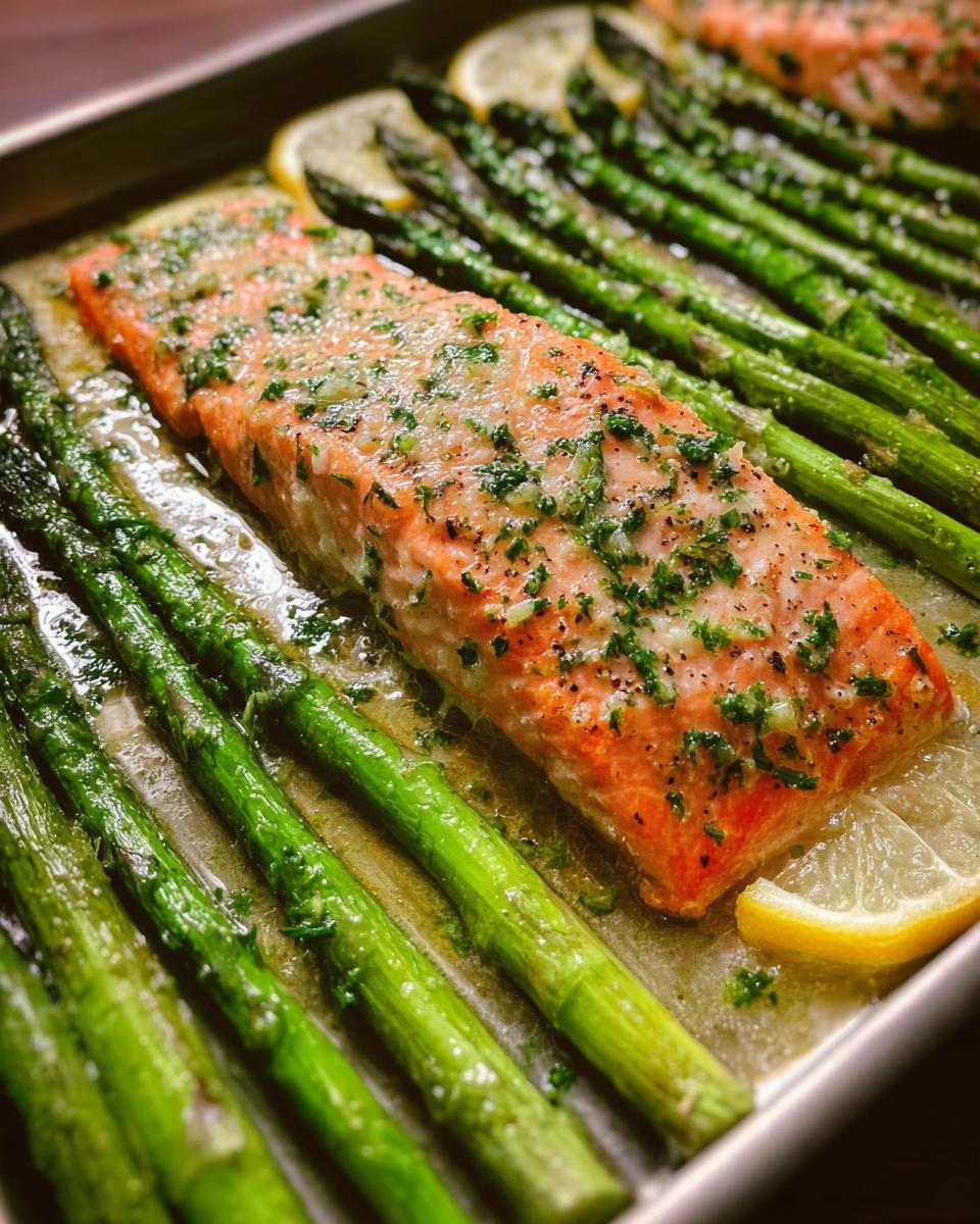 Close-up of a cooked salmon fillet covered in garlic butter sauce next to bright green asparagus spears.