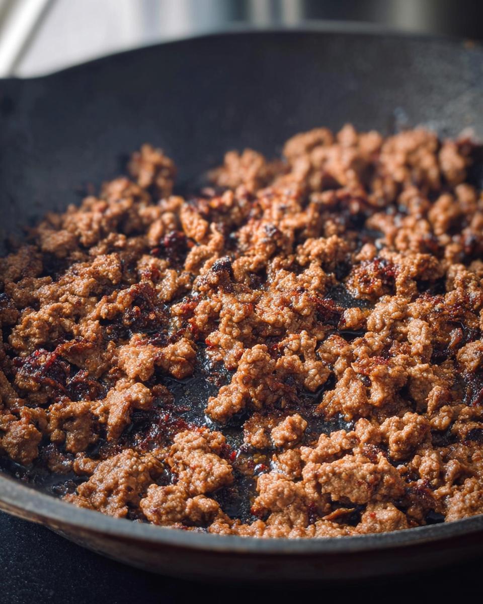Close-up of browned ground beef cooking in a cast-iron skillet, a key ingredient in many ultimate ground beef recipes.