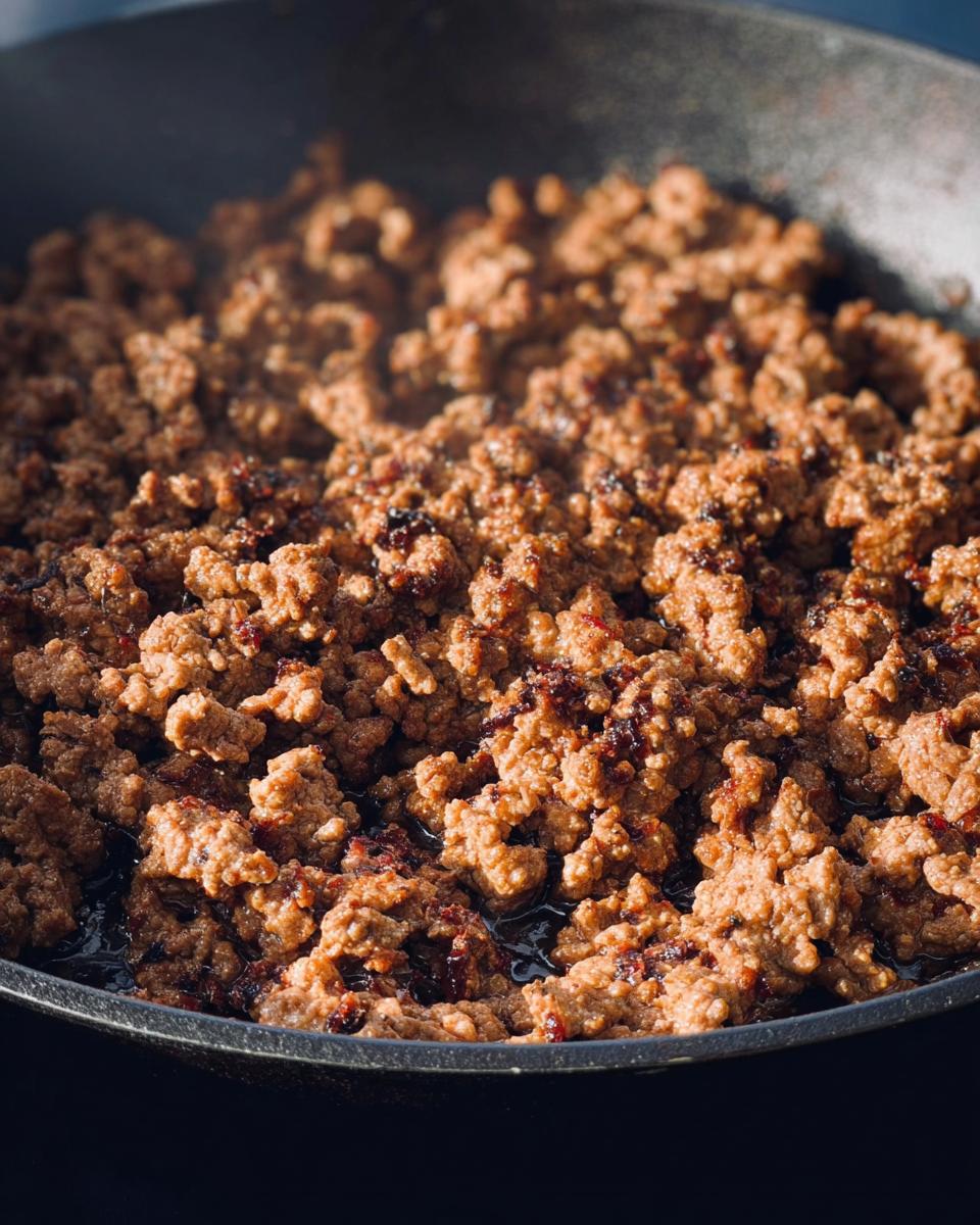 Close-up of ground beef browning in a cast iron skillet, showing texture and rendered fat.