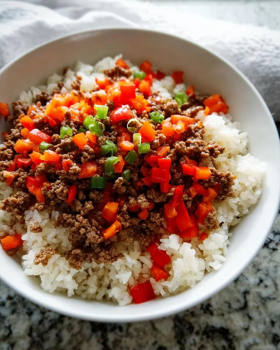 A bowl of white rice topped with seasoned ground beef, diced red bell peppers, and chopped green onions.