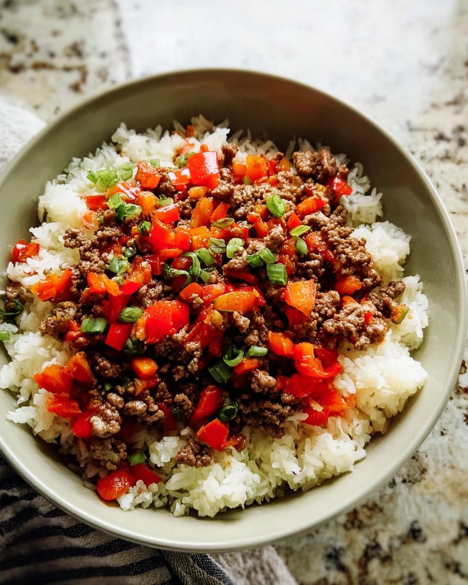 A bowl of fluffy white rice topped with seasoned ground beef and diced red bell peppers, garnished with green onions. A perfect example of ground beef recipes for busy weeknights.