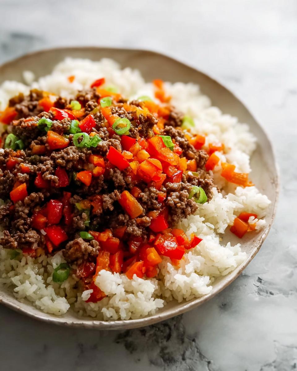 A close-up of a bowl featuring fluffy white rice topped with savory ground beef and diced red and orange bell peppers, garnished with green onions. This is one of our favorite Ground Beef Recipes for Busy Weeknights.