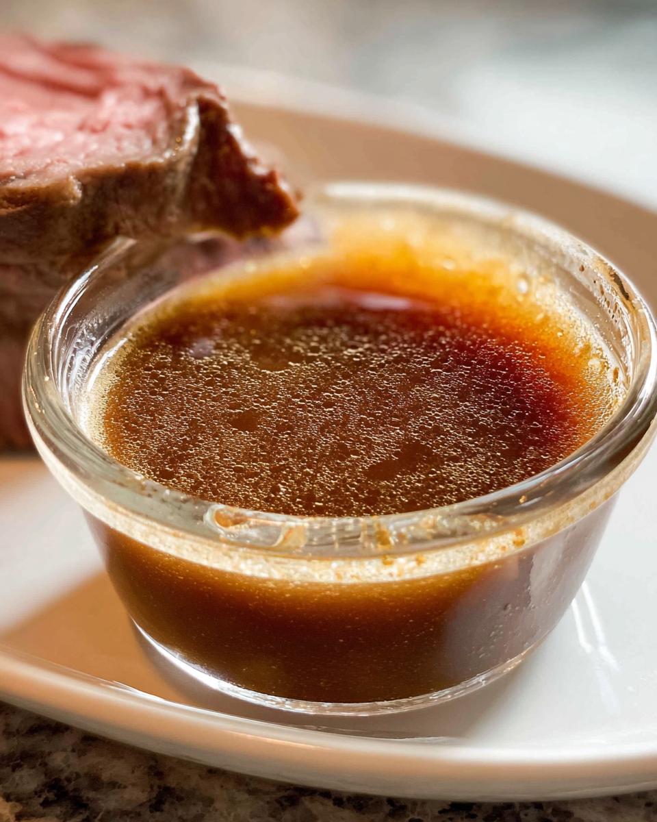 Close-up of rich, dark Homemade Au Jus without drippings served in a small glass ramekin next to a slice of roast beef.