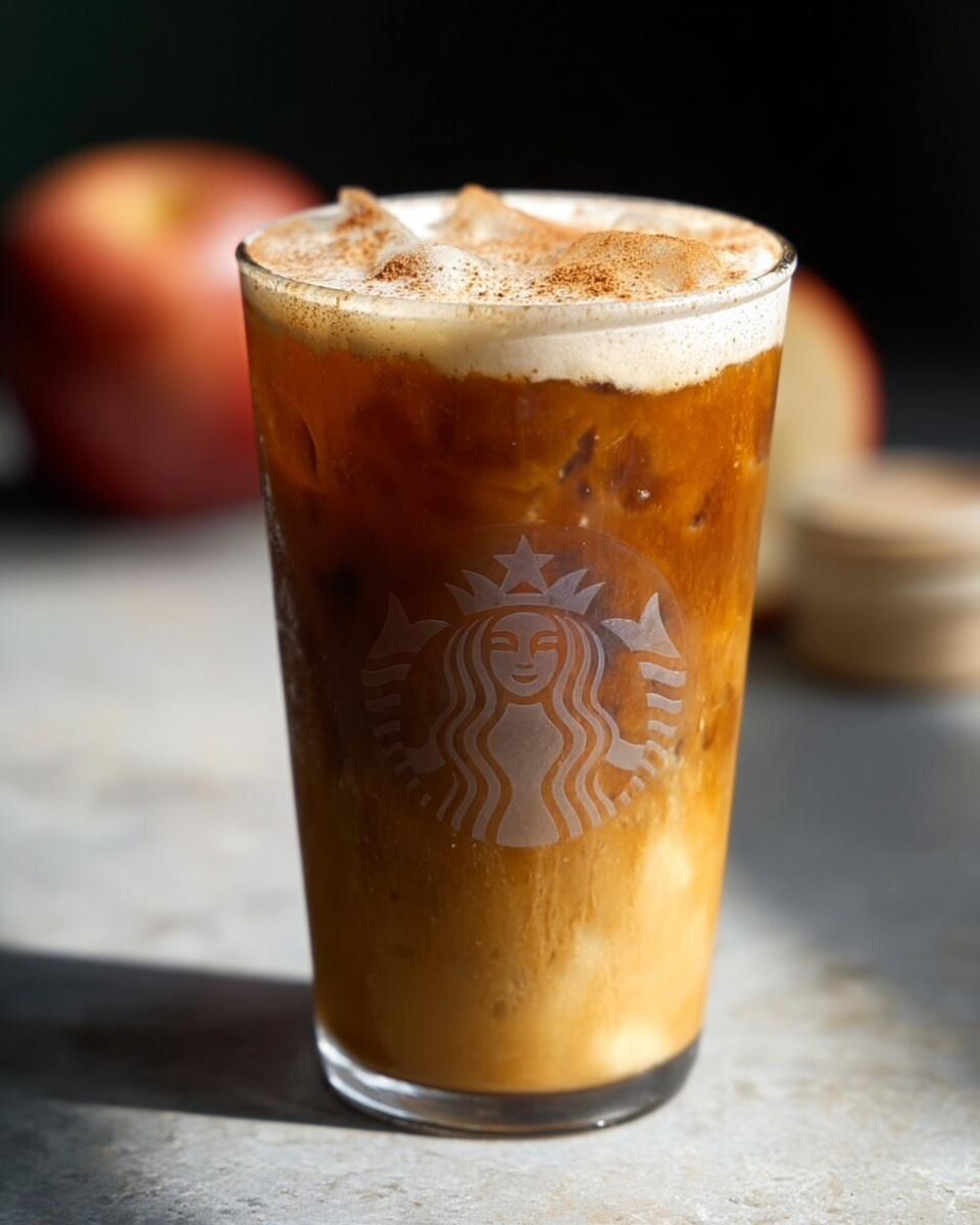 Close-up of an iced pumpkin spice latte in a Starbucks glass, topped with whipped cream and cinnamon.