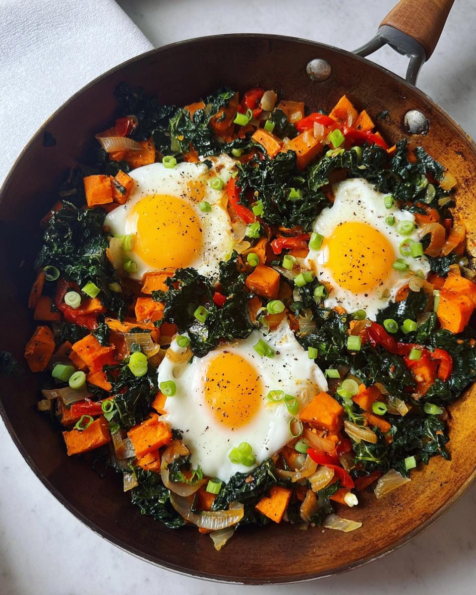 A vibrant one-pan breakfast with fried eggs nestled in a colorful hash of sweet potatoes, kale, and red peppers.