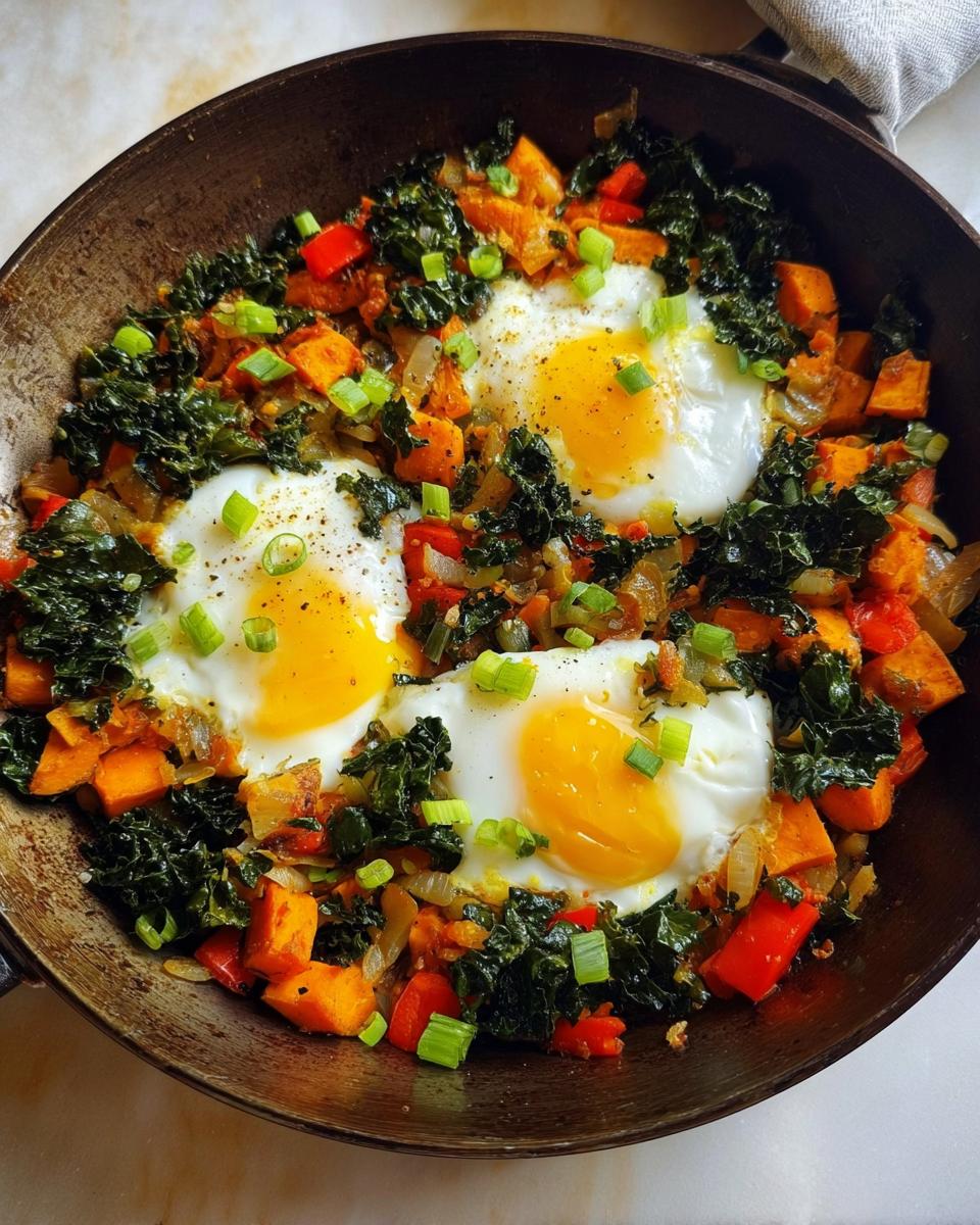 A vibrant one-pan breakfast featuring fried eggs nestled in a colorful hash of sweet potatoes, kale, red peppers, and onions, garnished with scallions.