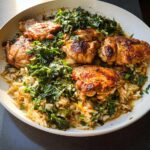 A close-up of a one-pan chicken thigh recipe featuring golden-brown chicken thighs served over seasoned rice with wilted greens.