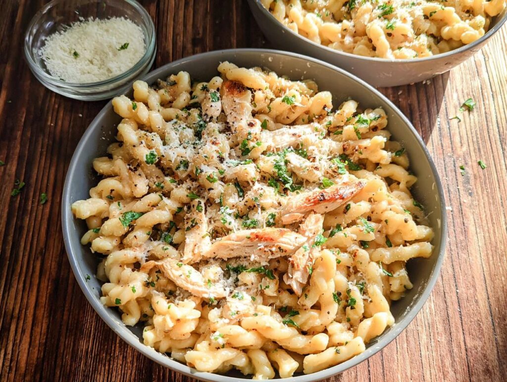 A close-up of One Pan Creamy Garlic Parmesan Chicken Pasta topped with shredded chicken, grated cheese, and parsley.