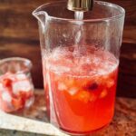 A pitcher filled with a vibrant red strawberry drink, ice, and fruit pieces, part of a one-pan Starbucks drink recipe.
