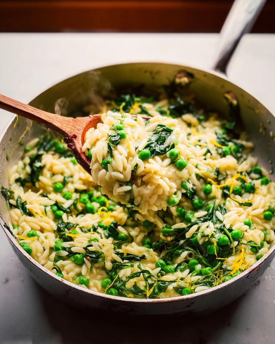 A wooden spoon scooping creamy orzo pasta with bright green peas and wilted spinach, a perfect 20 minute dinner idea.
