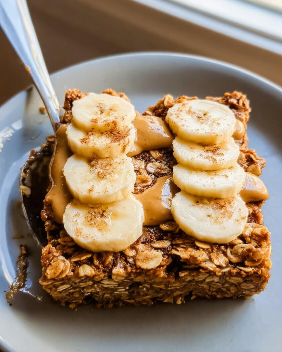 A slice of baked oatmeal topped with peanut butter, sliced bananas, and cinnamon, showcasing a perfect breakfast idea.