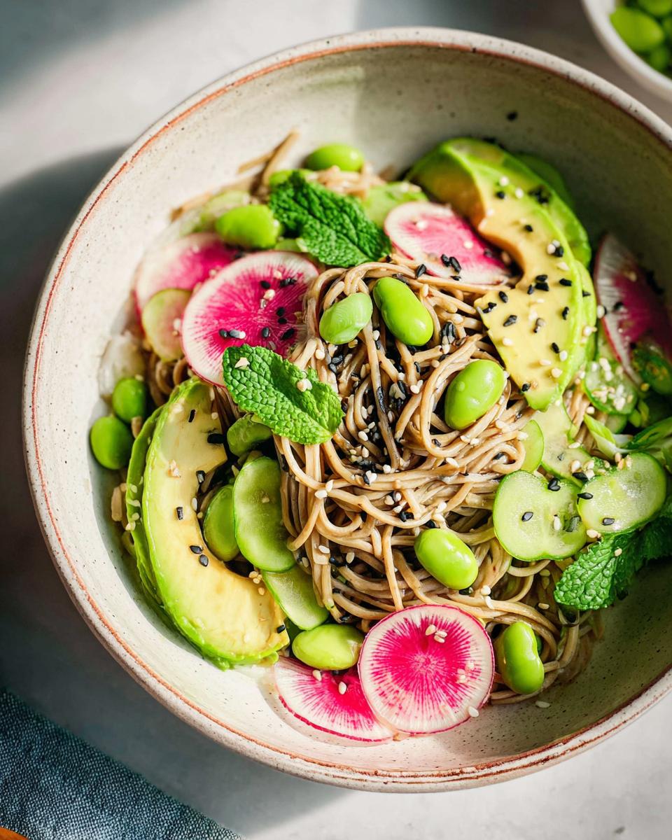 Close-up of a vibrant soba noodle salad with avocado, edamame, watermelon radish, and mint, a perfect dinner idea.