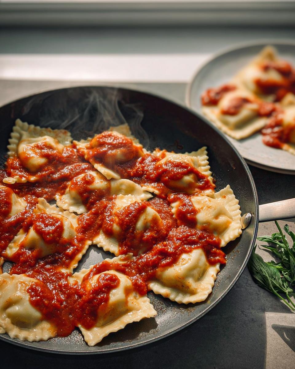 Close-up of steaming ravioli in a pan, generously topped with marinara sauce, showcasing perfect pasta recipes.