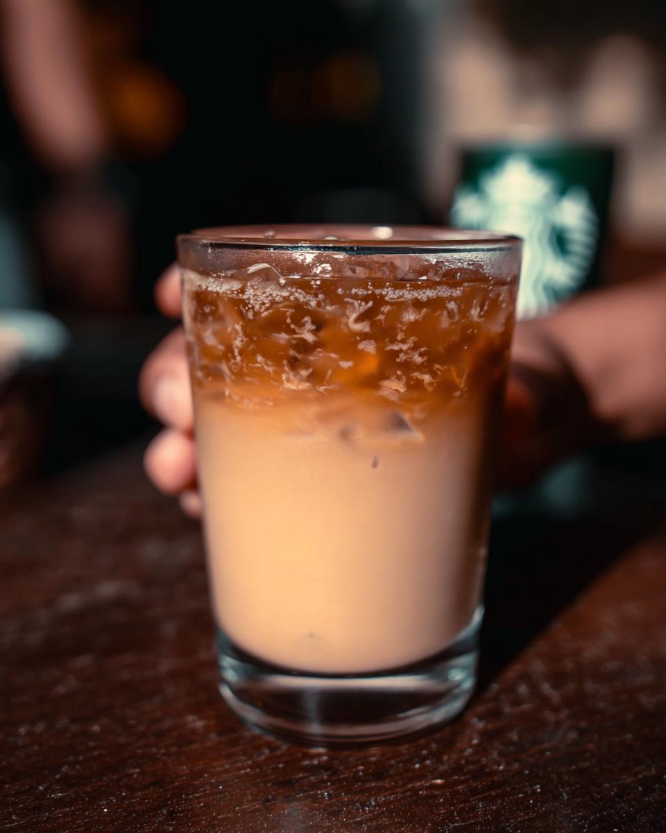 Close-up of a perfect Starbucks drink with ice, cream, and coffee layers, held by a hand.