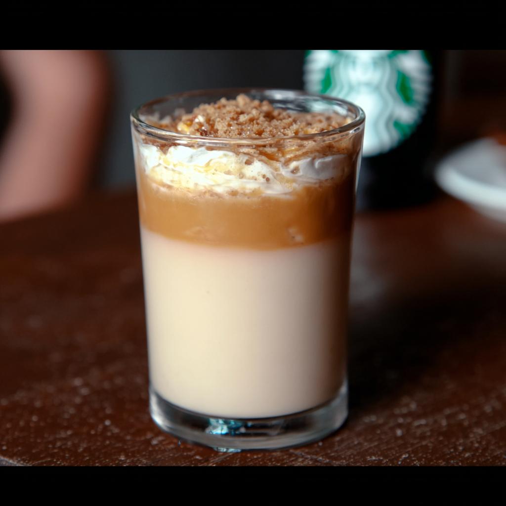 A layered Starbucks drink with milk, caramel, whipped cream, and crumble topping.