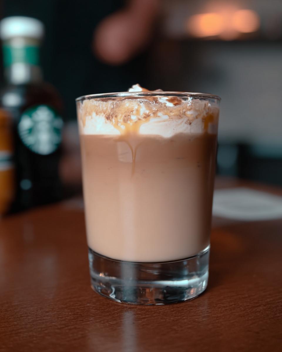 A close-up of a Starbucks drink with whipped cream, caramel drizzle, and cinnamon on top.