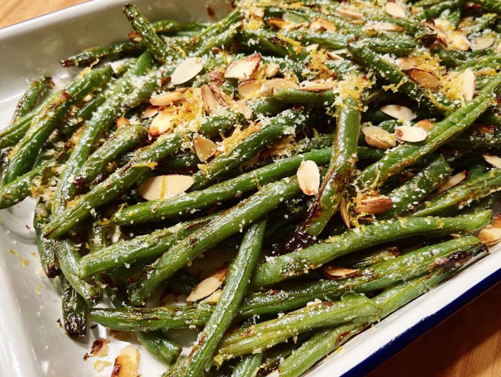 Close-up of perfectly cooked Thanksgiving green beans, topped with toasted almonds and lemon zest.