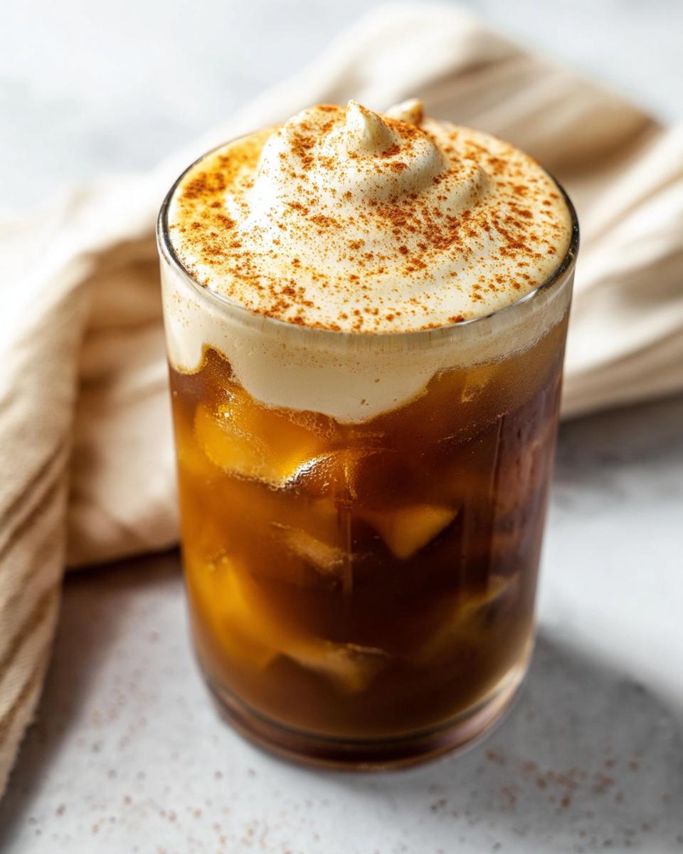 A tall glass filled with ice and cold brew coffee, topped with thick pumpkin cream and a dusting of spice, resembling a Pumpkin Cream Cold Brew.