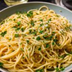 A close-up of a bowl of spaghetti, a quick pasta recipe, topped with fresh parsley and grated cheese.