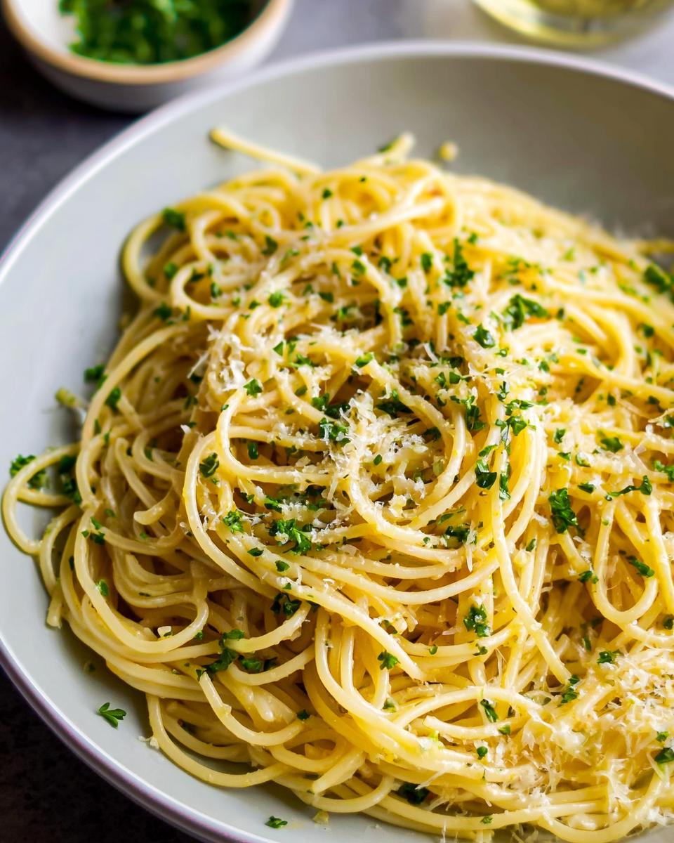 A close-up of a bowl of spaghetti tossed with garlic, parsley, and grated cheese, perfect for quick pasta recipes.