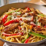 Close-up of restaurant-style Cajun chicken pasta with fettuccine, bell peppers, and shredded cheese.