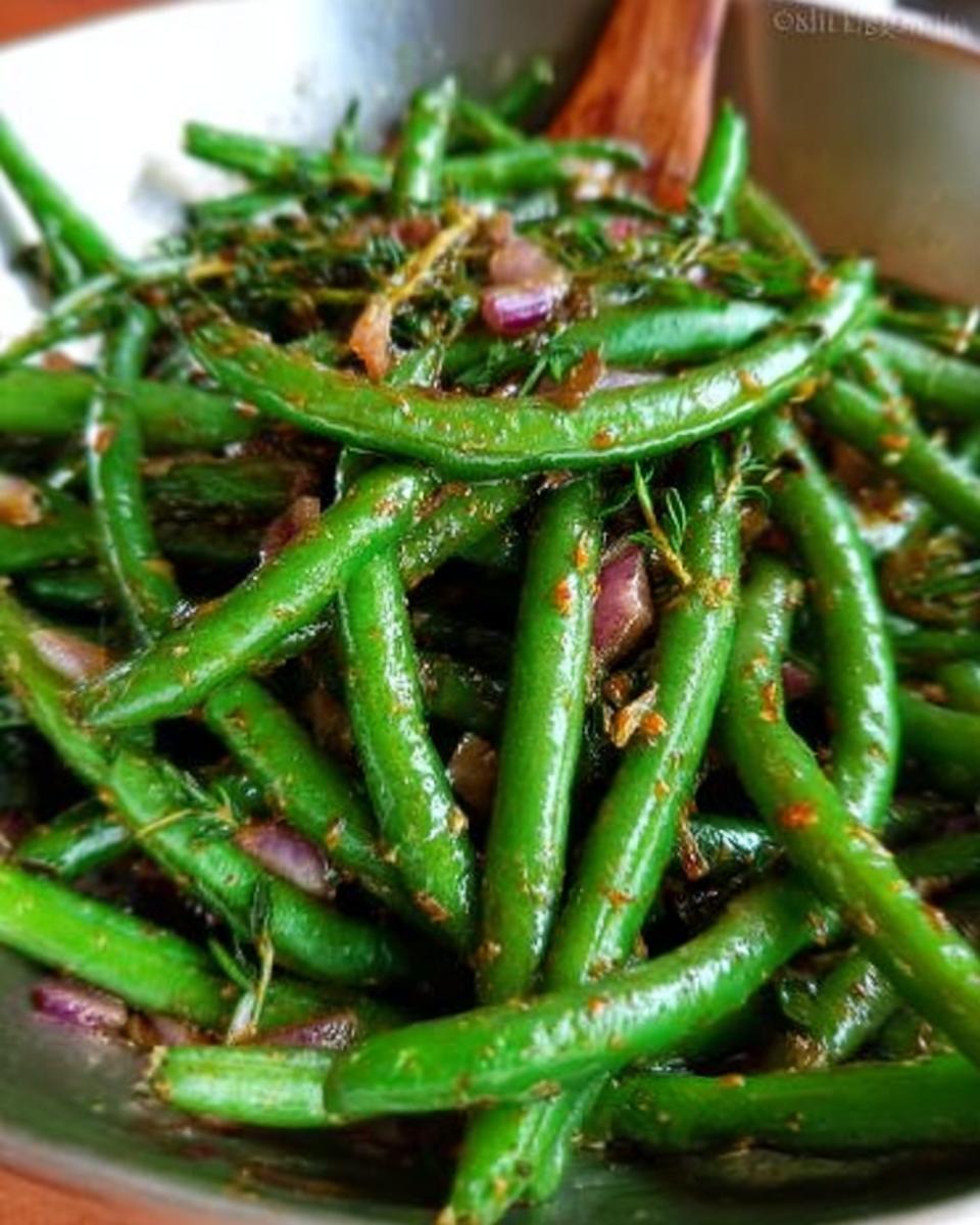 Close-up of glossy, vibrant green beans seasoned with red onion and herbs, ready for Thanksgiving dinner.