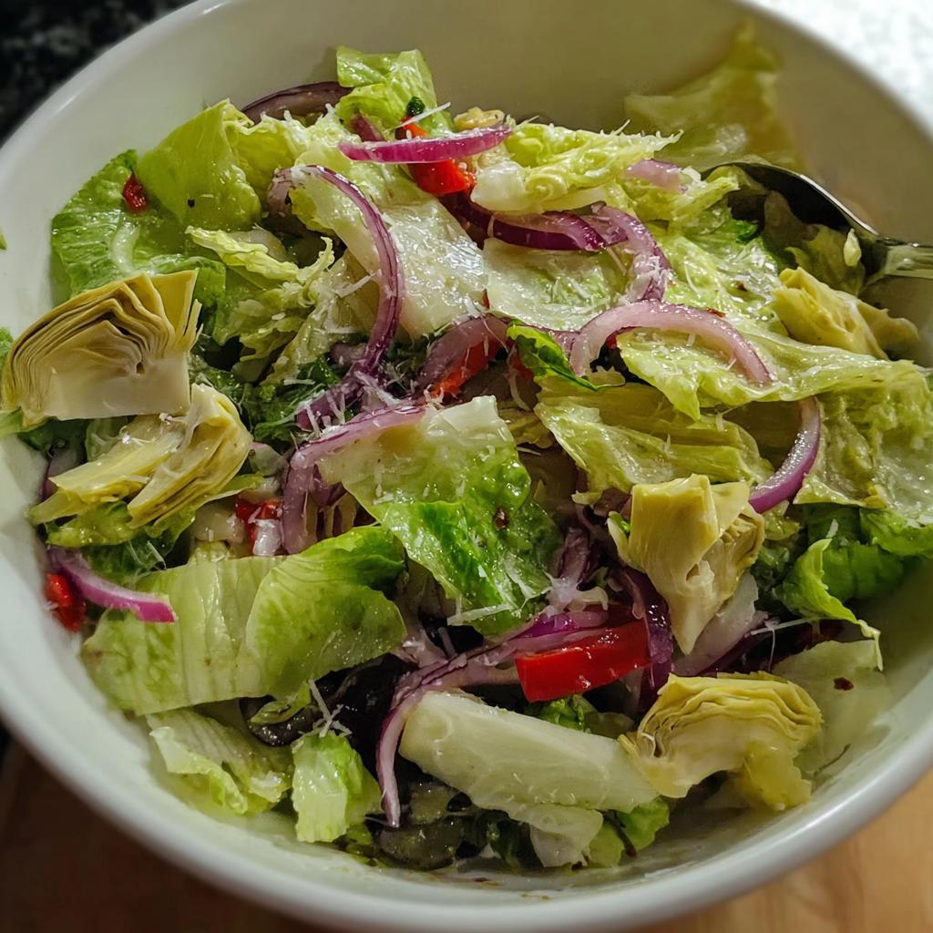 A vibrant bowl of Restaurant-Style Thanksgiving Salad with crisp lettuce, red onion, artichoke hearts, and red bell pepper.
