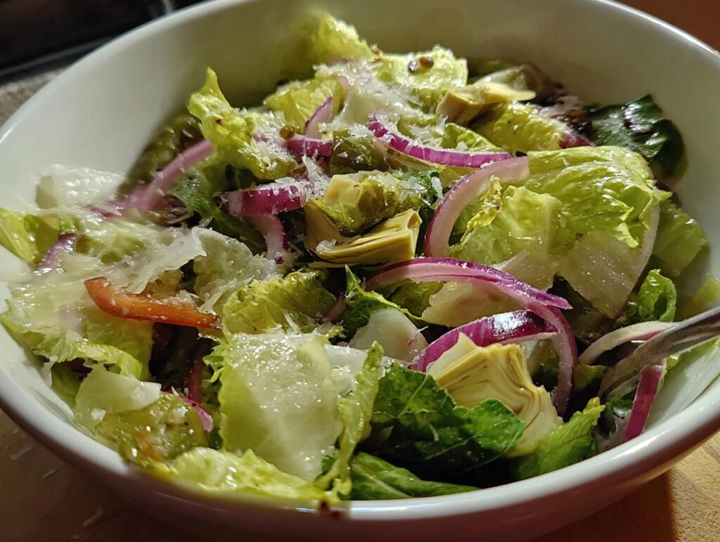 A close-up of a restaurant-style Thanksgiving salad featuring crisp romaine lettuce, red onion, artichoke hearts, and shaved parmesan.