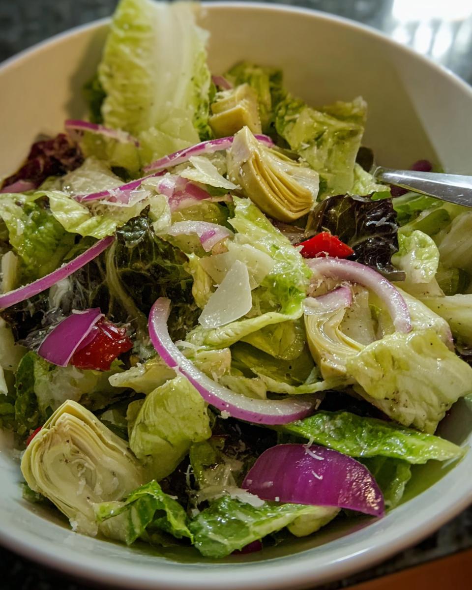 Close-up of a restaurant-style Thanksgiving salad featuring crisp lettuce, artichoke hearts, red onion, and shaved parmesan.