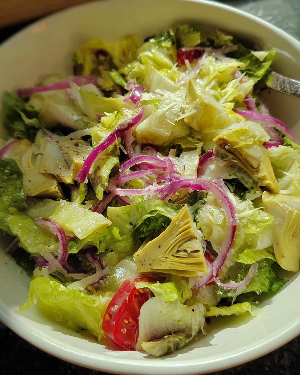 Close-up of a vibrant Restaurant-Style Thanksgiving Salad with romaine lettuce, red onion, artichoke hearts, and cherry tomatoes.