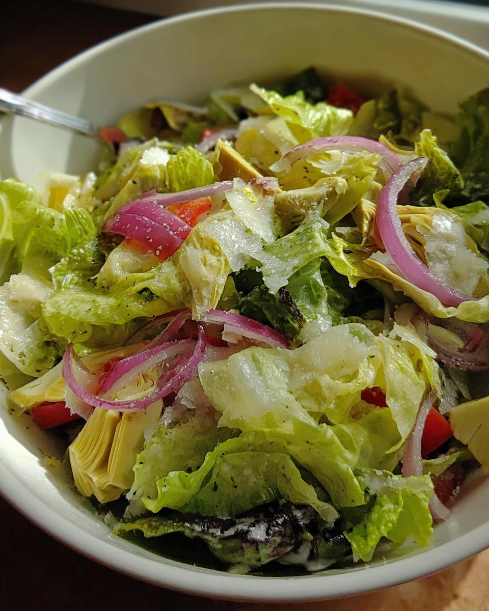 Close-up of a vibrant Restaurant-Style Thanksgiving Salad with romaine lettuce, red onion, artichoke hearts, and shaved parmesan.