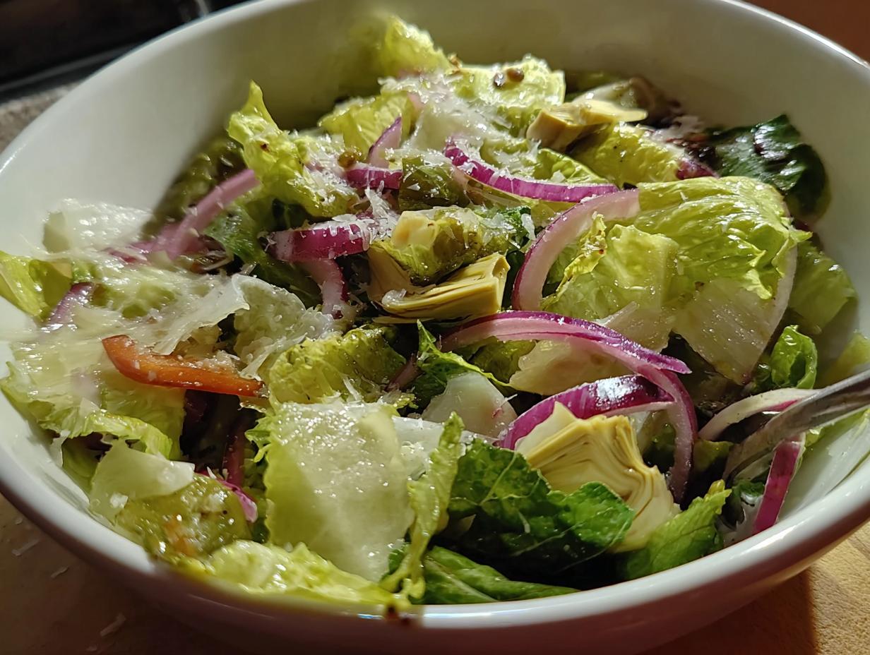 A close-up of a restaurant-style Thanksgiving salad featuring crisp romaine lettuce, red onion, artichoke hearts, and shaved parmesan.