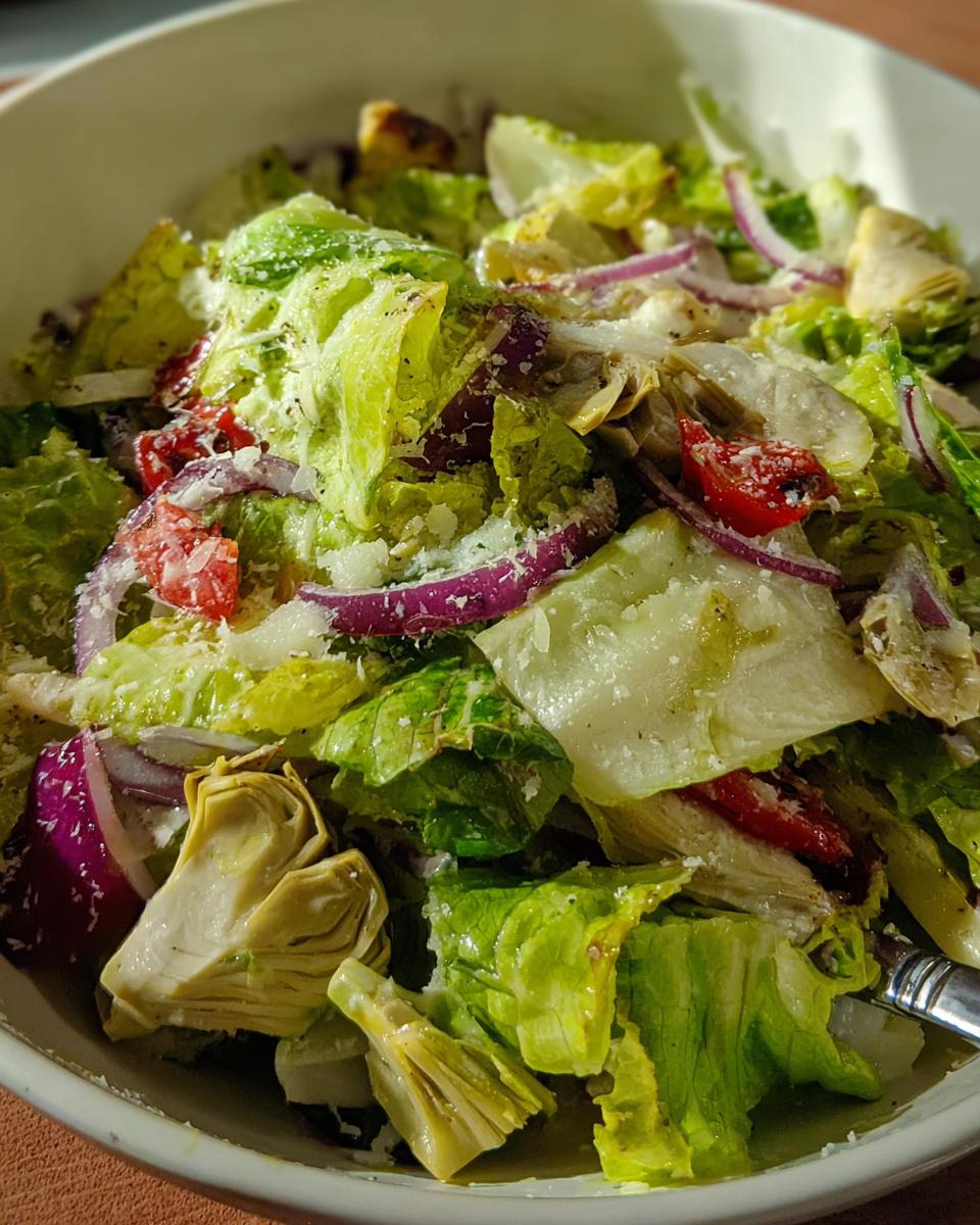 A close-up of a restaurant-style Thanksgiving salad featuring crisp lettuce, artichoke hearts, red onion, and cherry tomatoes, topped with parmesan.