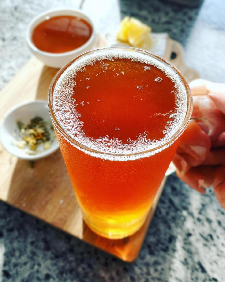 Close-up of a tall glass filled with a refreshing amber-colored Starbucks drink, topped with foam.
