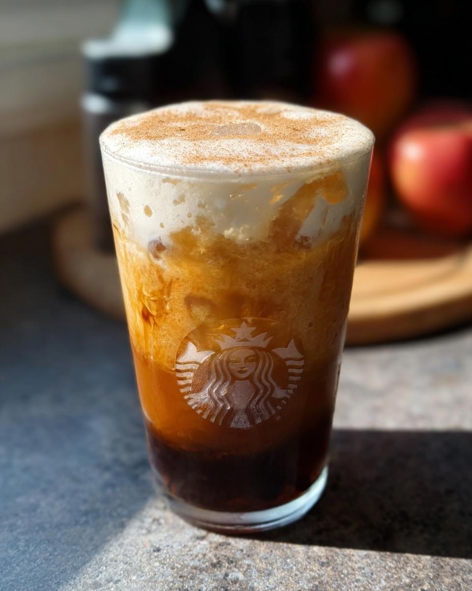 Close-up of a Starbucks Pumpkin Spice Latte with whipped cream and cinnamon, showcasing the Starbucks logo on the glass.